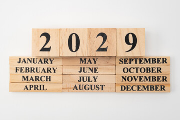 Year 2029 written on wooden cubes on top of the months of the year written on twelve rectangular pieces of wood. Isolated on white background - obrazy, fototapety, plakaty