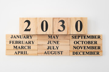 Year 2030 written on wooden cubes on top of the months of the year written on twelve rectangular pieces of wood. Isolated on white background