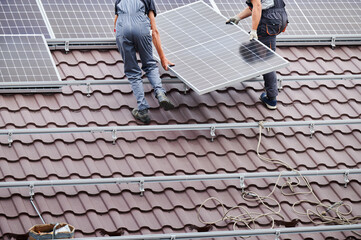 Men technicians carrying photovoltaic solar moduls on roof of house. Cropped view of engineers...