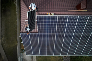 Men technicians mounting photovoltaic solar moduls on roof of house. Engineers in helmet installing...