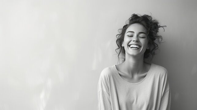 A joyful young woman in grayscale, standing against a minimalist coral-colored backdrop, her smile capturing a moment of pure happiness