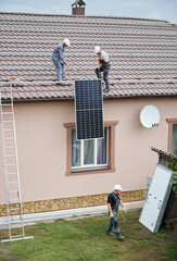 Men workers lifting up photovoltaic solar modul on roof of house. Electricians in helmets installing solar panel system outdoors. Concept of alternative and renewable energy.