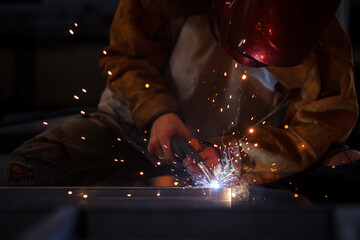 Heavy industry duty worker using a welding torch welds an iron steel in factory.