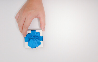 Hand holding a white gift box with a blue ribbon orange background with copy space. Free space for posting messages, advertisements, happy moments concept.