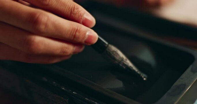 Hand, closeup of brush in ink for writing and calligraphy or ancient stationery for art and inkstone. Japanese creativity, black paint with paintbrush and person stroke with traditional vintage tools