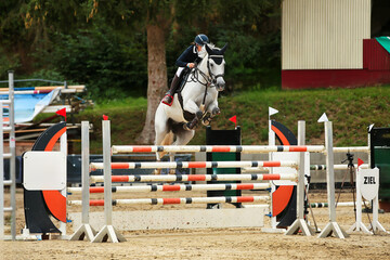 White horse with female rider jumping over a triple bar..