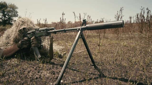 A close-up of a sniper wearing a camouflage suit or grass cloak, waiting and looking through a rifle scope. The sniper aims and shoots. Marksmanship shooting. Cinematic shot
