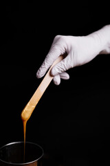 depilation and beauty concept - golden sugar paste or wax for hair removing with wooden waxing spatula sticks in hand in white latex gloves, beauty industry, concept of smooth skin