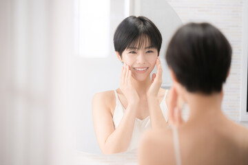 A beautiful woman looking in the mirror at a washbasin that is easy to use for beauty and other images, touching her cheeks with both hands while looking at the camera. 