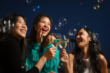 Obraz premium Group of cheerful female friends having fun toasting champagne and laughing together at the rooftop night outdoor party.