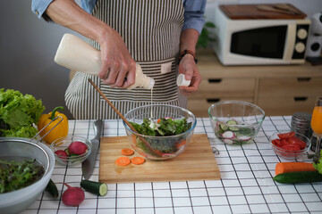 Cropped shot senior man pouring sauce into bowl with fresh salad. Healthy eating and culinary concept.