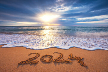 Sea sunrise over tropical island beach and handwritten text in sand new year 2024 - obrazy, fototapety, plakaty