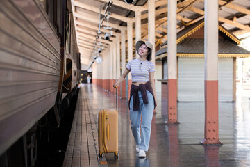 Fototapeta na wymiar Young woman wearing an explorer's hat and carrying a suitcase Stand and look for a train at the train station. Traveler's concept