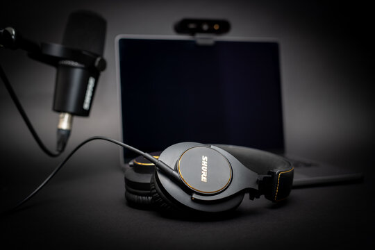 Podcast Setting with Shure microphone and headphones in front of black background with laptop and webcam