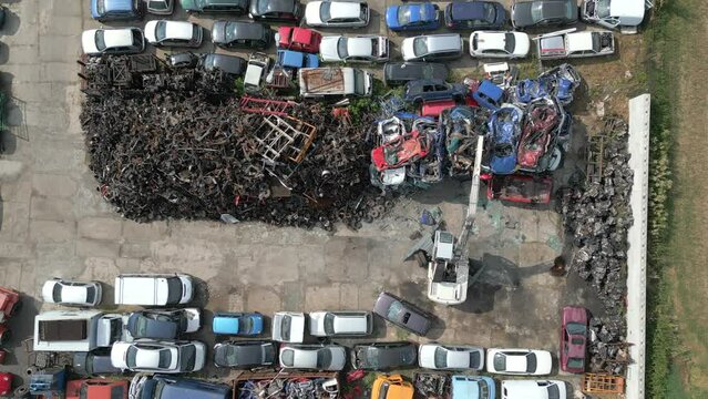 Top view of crane lifting scrap metal cars in a junkyard.