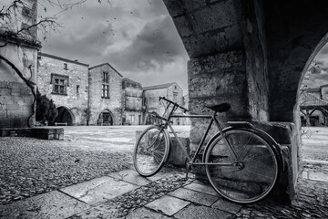 Black and white image of a bicycle under the covered walkway surrounding the market square of the 13th century bastide of Monpazier in the Dordogne region of France