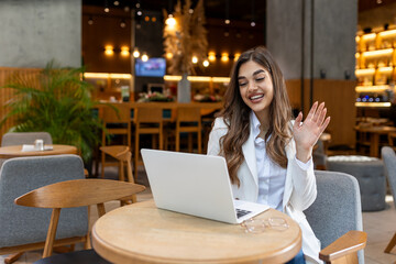 Positive young woman enjoying friendly video call on laptop computer using web camera for...