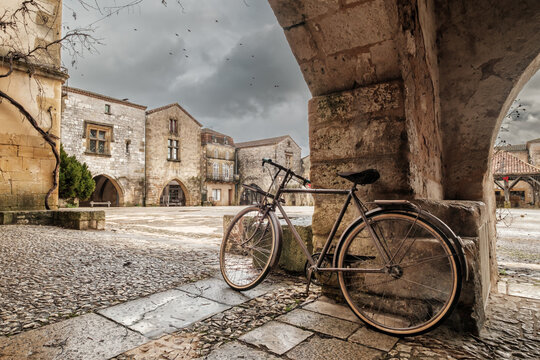 A bicycle under the covered walkway surrounding the market square of the 13th century bastide of Monpazier in the Dordogne region of France