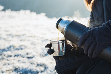 Hot tea poured from a thermos into a mug, cold winter, warm up with warm drinks, hiking in the...