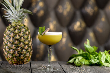 cocktail of green color decorated with a fox with a clothespin on a wooden board with basil leaves and pineapple