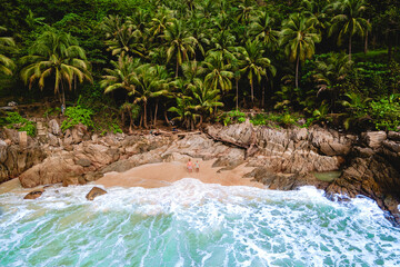 A couple of men and women relaxing on a white tropical beach with palm trees in Phuket Thailand