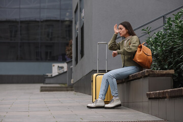 Being late. Worried woman with suitcase sitting on bench outdoors, space for text