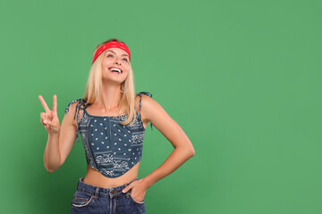 Portrait of happy hippie woman showing peace sign on green background. Space for text