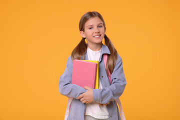 Obraz premium Happy schoolgirl with books on orange background