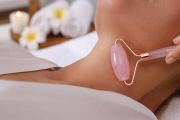 Naklejka premium Woman receiving facial massage with rose quartz roller in beauty salon, closeup