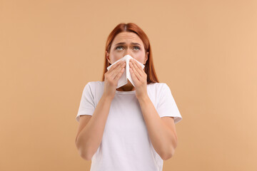 Suffering from allergy. Young woman with tissue sneezing on beige background