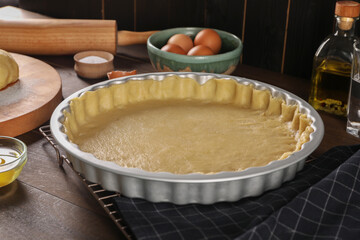 Pie tin with fresh dough and ingredients on wooden table. Making quiche