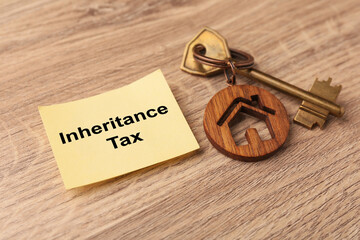 Inheritance Tax. Paper note and key with key chain in shape of house on wooden table, closeup