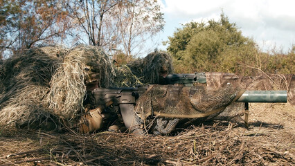 Fototapeta na wymiar Snipers in an ambush in the grass, disguised as terrain on an anti-terrorist operation with sniper rifles, shooting at the enemy. Footage of military operations. Soldiers in full gear. Cinematic shot