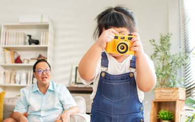 Asian little girl playing with family camera toy with concentration, taking photo shot with fun, standing in cozy living room at home. Education, Kid, Activity, Interior house Concept.