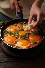 Woman dipping piece of bread into delicious Shakshuka at wooden table, closeup