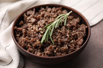 Fried ground meat in bowl and rosemary on brown textured table, closeup