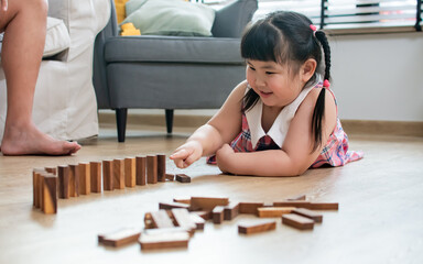 Asian little cute girl wearing pink dress, playing wooden block toys game with family, smiling with...