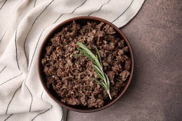 Fried ground meat in bowl and rosemary on brown textured table, top view