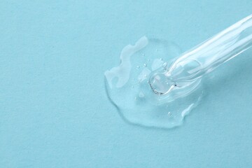 Dripping cosmetic serum from pipette onto light blue background, top view. Space for text