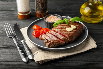 Delicious grilled beef steak served with spices and tomatoes on black wooden table