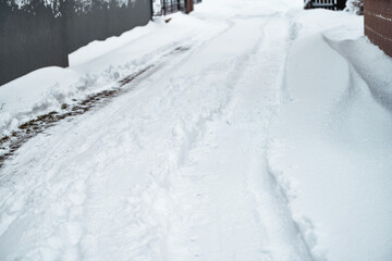 A plowed road in a snowy landscape. The aftermath of a blizzard. The trees and rocks are covered with white snow. A blizzard has left a thick layer of snow on the ground and the trees.