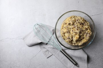 Chocolate chip cookie dough in bowl and whisk on light gray table, flat lay. Space for text