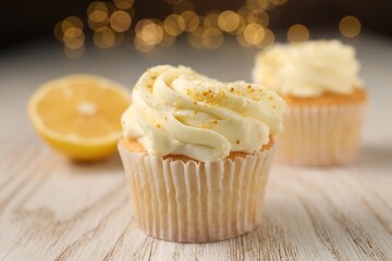 Tasty cupcakes with cream and lemon zest on white wooden table, closeup
