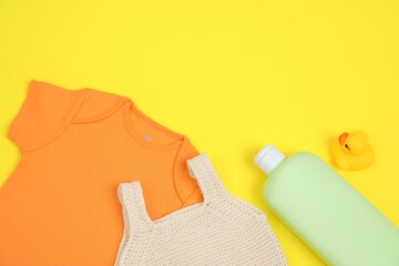 Bottles of laundry detergents, baby clothes and rubber duck on yellow background, flat lay. Space...