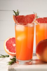 Tasty grapefruit drink with ice in glasses, rosemary and fresh fruits on light table