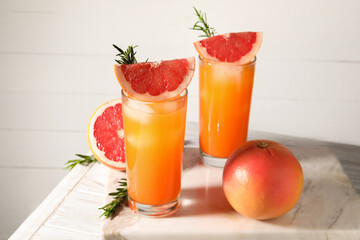 Tasty grapefruit drink with ice in glasses, rosemary and fresh fruits on light wooden table