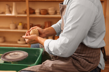 Man crafting with clay over potter's wheel indoors, closeup