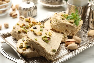 Tasty halva with pistachios and mint on white table, closeup