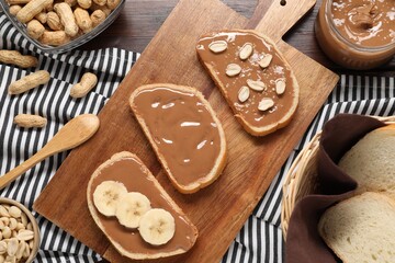 Toasts with tasty nut butter, banana slices and peanuts on wooden table, flat lay