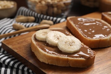 Toasts with tasty nut butter and banana slices on wooden board, closeup